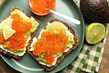 Delicious sandwiches with avocado, red caviar, cream cheese and lime on table, flat lay