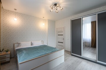 Cozy bedroom features a bed with a turquoise blanket, floral wallpaper, and a sliding door wardrobe. Warm lighting enhances the room's ambiance