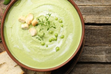 Tasty pea cream soup with croutons and thyme served on wooden table, top view