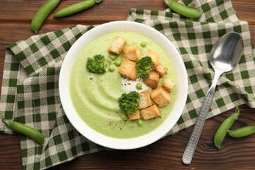Tasty pea cream soup with croutons and broccoli served on wooden table, flat lay