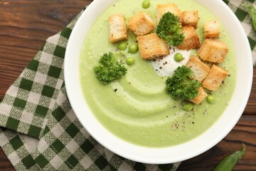Tasty pea cream soup with croutons and broccoli served on wooden table, top view