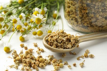 Dry and fresh chamomile flowers on white wooden table, closeup