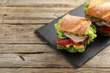 Tasty baguette sandwich with ham and vegetables on wooden table, closeup. Space for text