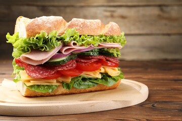 Tasty baguette sandwich with ham and vegetables on wooden table, closeup