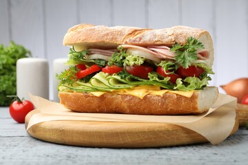 Tasty baguette sandwich with ham, cheese and vegetables on grey wooden table, closeup