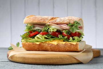 Tasty baguette sandwich with ham, cheese and vegetables on grey wooden table, closeup
