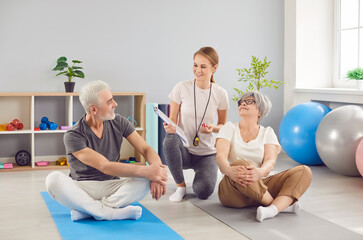 Female happy doctor or trainer communicates with a senior couple during a rehabilitation or physical therapy session. Professional support provided to elderly patients during recovery process.
