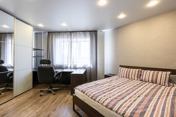 modern bedroom with a bed, desk, office chair, and closet. Natural light filters through the window, creating a bright and comfortable space