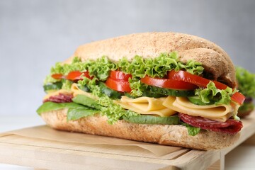Tasty baguette sandwich with smoked sausage, cheese and vegetables on white table, closeup