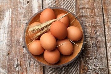 Raw eggs and spikes of wheat on wooden table, top view