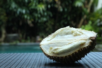 Fresh ripe durian on wicker table near swimming pool outdoors, closeup. Space for text
