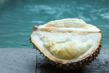 Fresh ripe durian on stone surface near swimming pool outdoors, closeup. Space for text