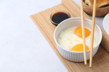Half-boiled eggs in bowl, soy sauce, chopsticks and toasted bread on light grey table, closeup. Space for text