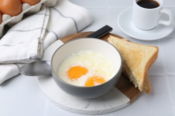 Half-boiled eggs in bowl, coffee and toasted bread on white tiled table, closeup