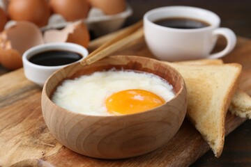 Half-boiled egg in bowl, soy sauce, chopsticks, coffee and toasted bread on table, closeup