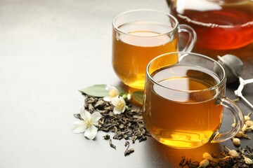 Aromatic jasmine tea in glass cups, brew and flowers on grey table, closeup. Space for text