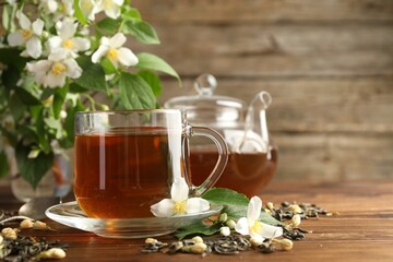 Aromatic jasmine tea in glass cups, teapot, brew and flowers on wooden table, closeup. Space for text