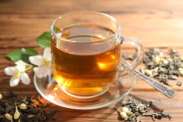 Aromatic jasmine tea in glass cup, brew and flowers on wooden table, closeup