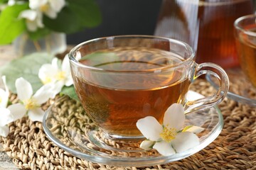 Aromatic jasmine tea in glass cup and flowers on table, closeup