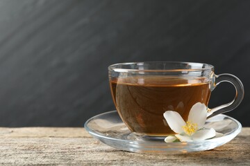 Aromatic jasmine tea in glass cup and flower on wooden table, closeup. Space for text