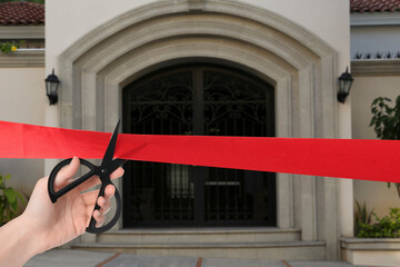 Woman cutting red ribbon at opening ceremony of house, closeup