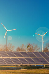 Industrial big solar power plant and wind turbines as universal green energy solution in Germany with direct sunlight and lens flare. Concept of energy and sustainable living.
