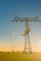Beautiful farm landscape and industrial high voltage power line pylons and wind turbines farm at sunset warm colors and direct sun light with lens flare and sun rays in Germany