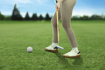 Woman with club playing golf on green course, closeup