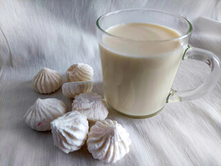 Airy meringue cookies and a mug of milk on light fabric, creating a cozy and homemade atmosphere.