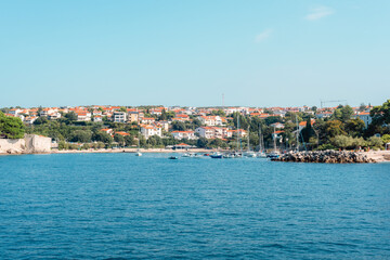 Fototapeta premium Coastal town with red-roof houses and boats docked near the shore under a clear blue sky. Krk island, Croatia