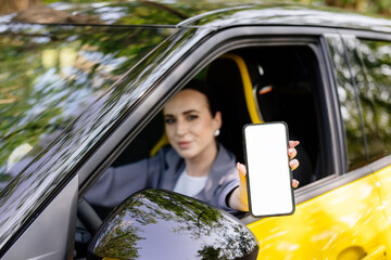 Happy woman demonstrates smartphone with white screen while sitting in car. Smiling woman showing a...