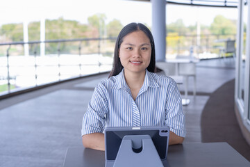 Young Asian woman working on tablet with stylus, focused and productive in a modern indoor/outdoor...