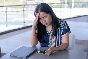 Anxious Asian woman experiencing a headache or stress while working on her tablet, capturing the challenges of remote work and mental strain in a contemporary setting
