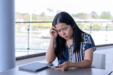 Anxious Asian woman experiencing a headache or stress while working on her tablet, capturing the...