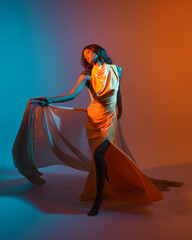 creative portrait of a female model wearing a glamorous yellow fashion ball gown. elegantly posing on studio background with dramatic colourful  lighting