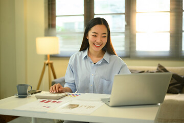 Cheerful female professional analyzing reports at a bright, modern home office desk with digital tools and documents