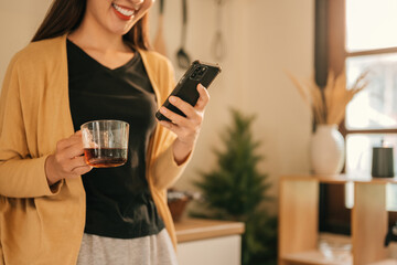 Cropped image of a Woman Enjoying Coffee and Checking Smartphone in Cozy Kitchen, Digital Morning Routine