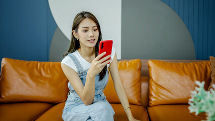 Happy asian young woman sit on sofa at home typing on mobile phone receive great news celebrating...