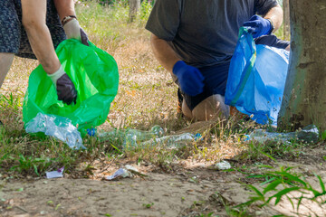 Naklejka premium One man and a senior woman as a volunteers cleaning up a forest, collecting plastic bottles and other garbage in bags.