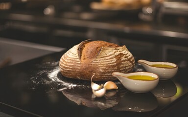 Still life with a loaf of bread, flour, oil and garlic on a black surface