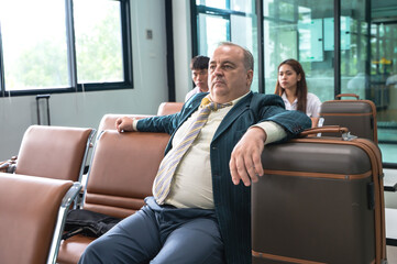 Senior businessman with suitcase  sitting in waiting hall in airport