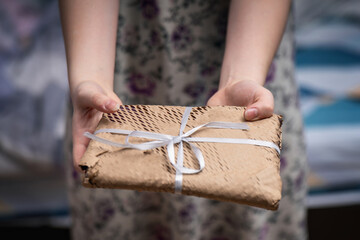Young woman offering a gift-wrapped book in craft perforated paper with a bow, showcasing thoughtful presentation