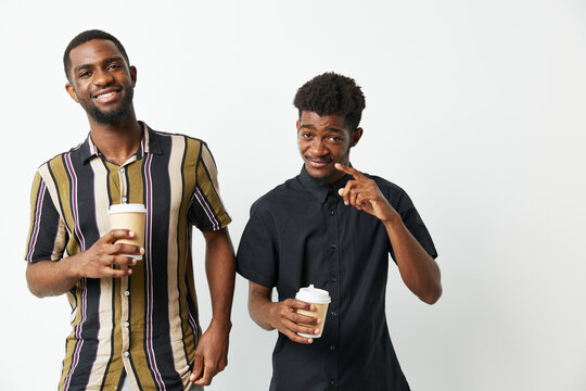 Two African American men smiling and enjoying coffee together. Their casual outfits and cheerful expressions create a warm and friendly atmosphere.
