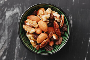 Mix of nuts in green ceramic bowl. Almonds walnuts and cashews closeup. Healthy protein snack food. Natural nutrition mix on marble table. Rustic diet ingredient. Vegetarian organic kitchen concept.