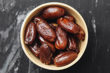 Sweet dried dates in a bowl. Natural exotic fruit snack. Healthy dessert alternative. Organic tropical date fruits. Tasty dried food in rustic brown dish. Vegetarian dried dates closeup.