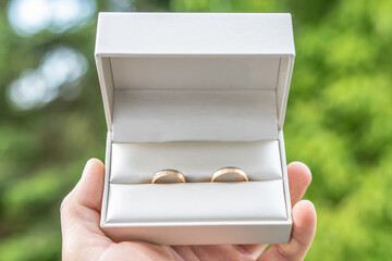 Elegant gold wedding rings lie among soft satin white ribbon. Front vertical view. Mockup for wedding postcard