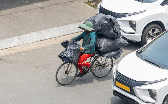 A person is riding a bicycle with full large garbage bags, through an urban street.