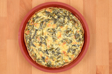 A top-down shot shows a freshly baked golden-brown spinach and cheese pie in a round red baking...