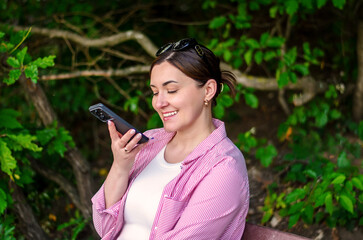 Smiling woman using voice message on smartphone in park