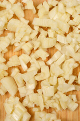 A detailed vertical close-up shot captures a texture of freshly minced garlic spread across a wooden surface, highlighting its irregular shapes